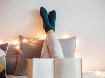 Young women relaxing in bad while reading book and enjoying in decorative light