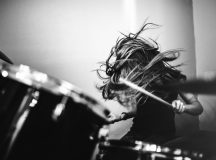 A 9 year old girl has fun playing a drum set in her room, working on songs for her band. High contrast black and white image.